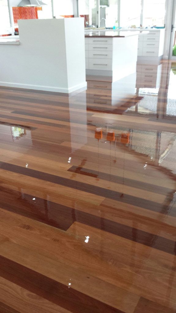 A Wooden Floor in a Room With a Kitchen in the Background — Timbertop Floor Sanding & Polishing In Bungalow, QLD