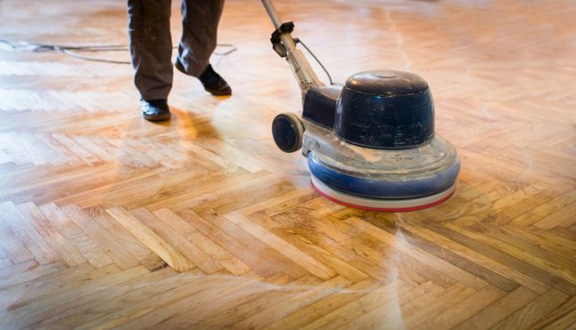 A Person is Polishing a Wooden Floor With a Machine — Timbertop Floor Sanding & Polishing In Bungalow, QLD