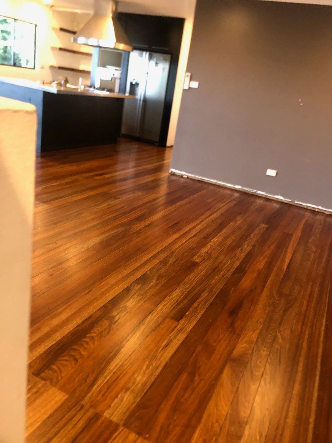 A Living Room With a Wooden Floor and a Kitchen in the Background — Timbertop Floor Sanding & Polishing In Bungalow, QLD