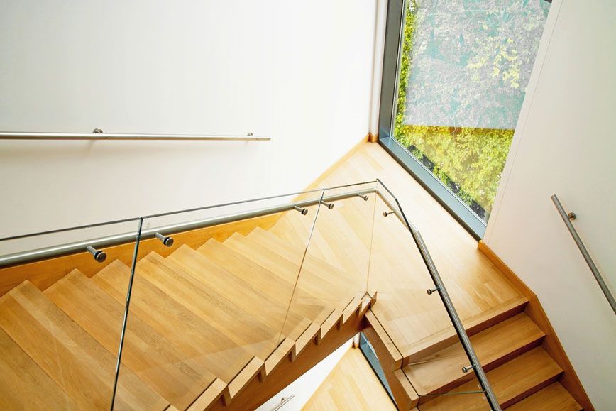A Wooden Staircase With a Glass Railing and a Window — Timbertop Floor Sanding & Polishing In Bungalow, QLD