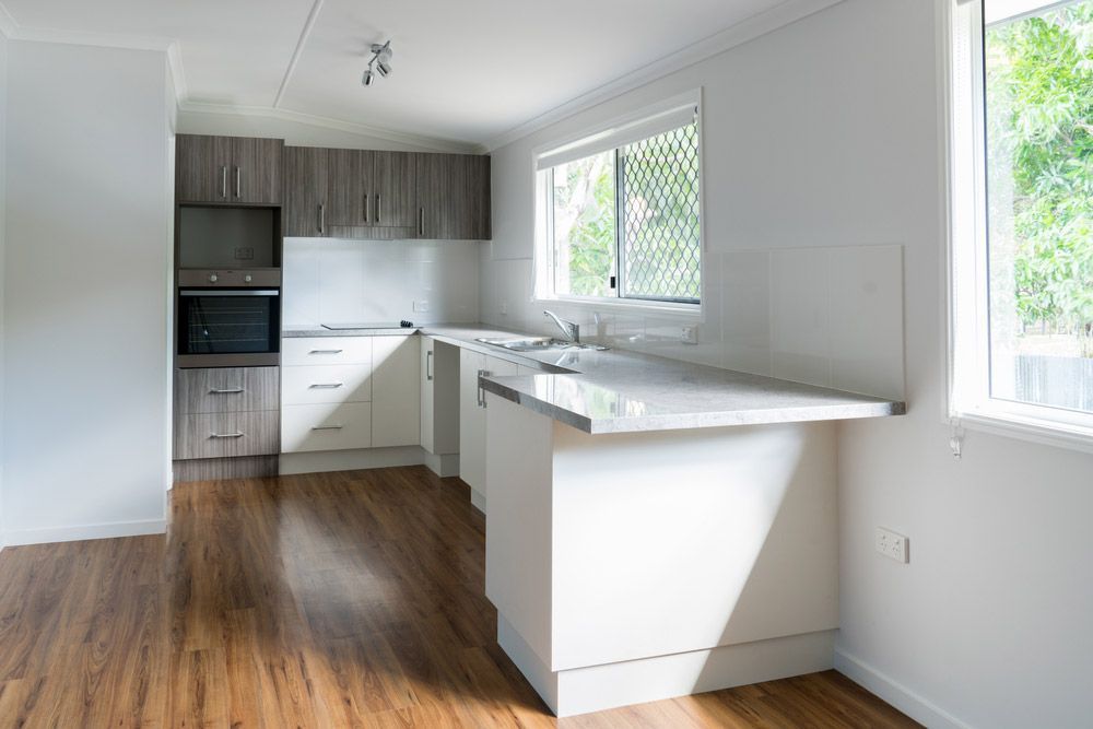 An Empty Kitchen With White Cabinets and Wooden Floors — Timbertop Floor Sanding & Polishing In Cairns, QLD