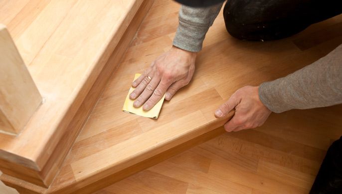 A Person is Sanding a Wooden Staircase With a Sandpaper — Timbertop Floor Sanding & Polishing In Bungalow, QLD