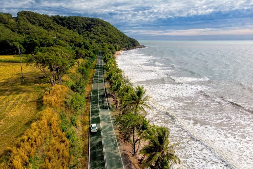An Aerial View of a Car Driving Down a Road Next to the Ocean — Timbertop Floor Sanding & Polishing In Port Douglas, QLD