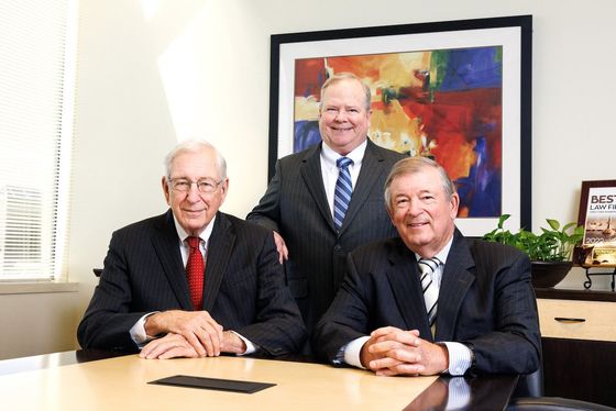 Three men in suits and ties are posing for a picture while sitting at a table.