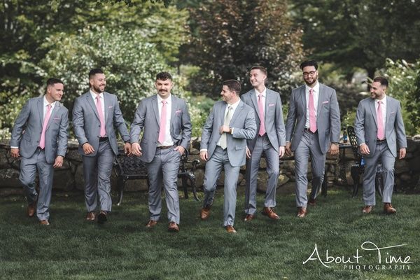 Group of men in gray suits and pink ties walking outdoors on grass at a formal event