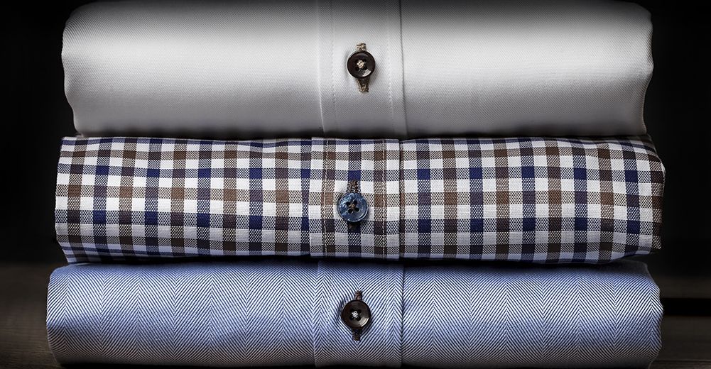 Three folded dress shirts stacked vertically: silver, blue-and-white checkered, and light blue.