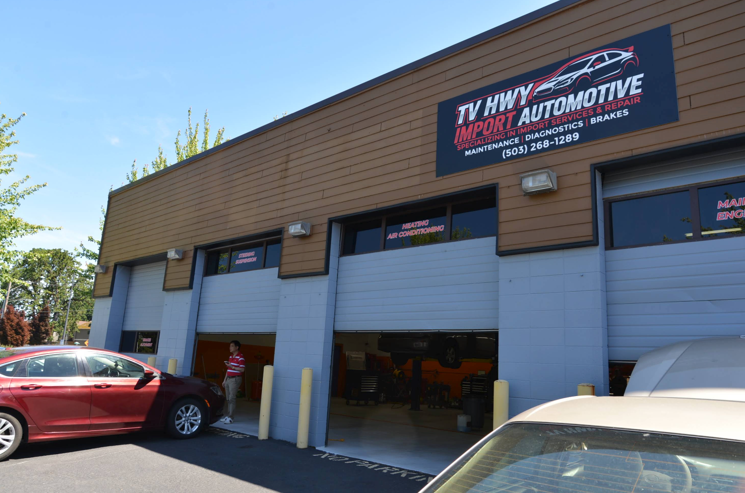 Auto repair shop exterior with open garage doors and parked cars in front | TV HWY Import Automotive