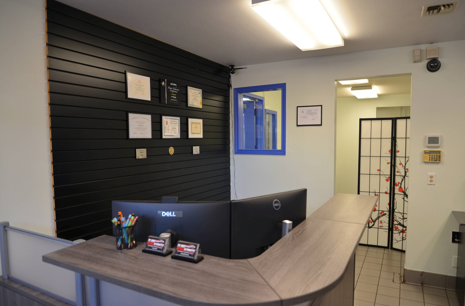 Front desk reception area with a curved counter, black slat wall, and blue-framed window | TV HWY Import Automotive