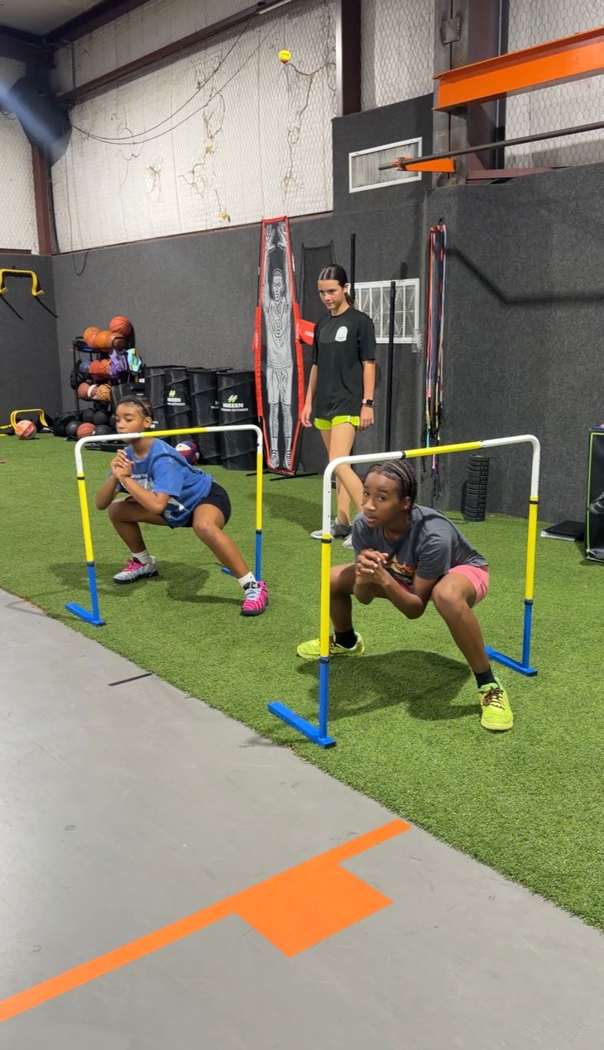 Two athletes doing low hurdle drills in an indoor gym on turf