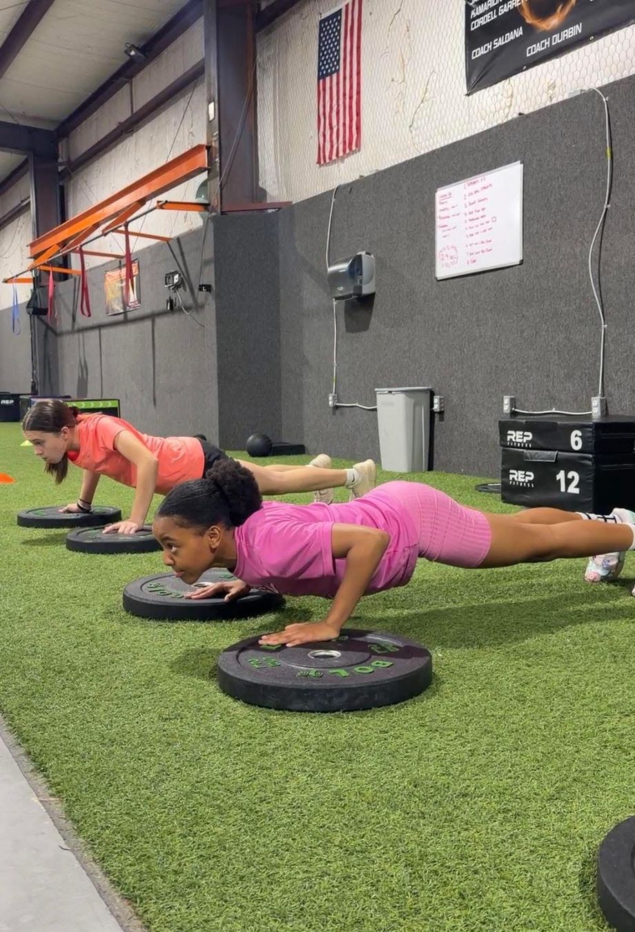 Youth athletes doing push-ups on weight plates in a gym on green turf.