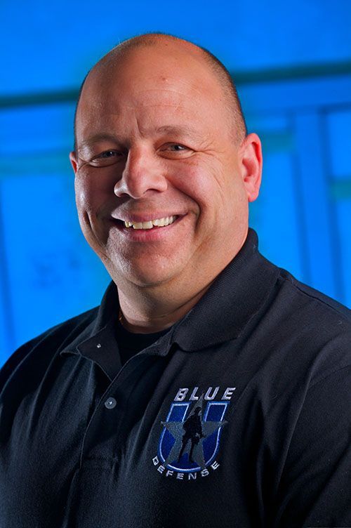 Man with bald head, smiling, wearing a black polo shirt with 