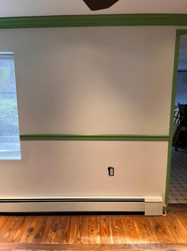 A living room with hardwood floors and a white wall with green trim.