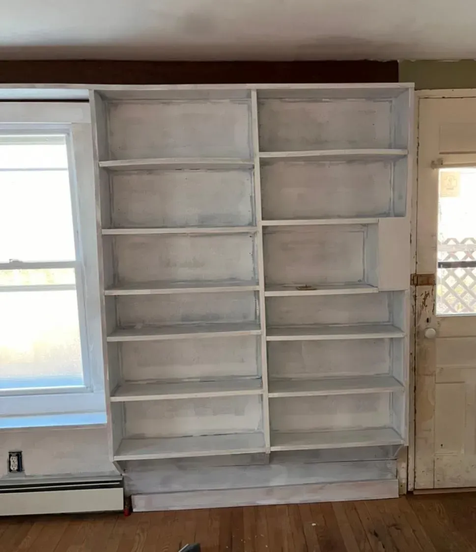 A large white bookshelf in a living room next to a window.