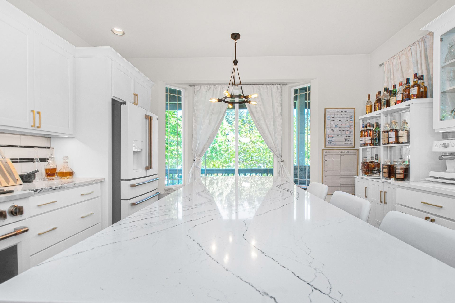 A kitchen with white cabinets , a large table , and a large window.