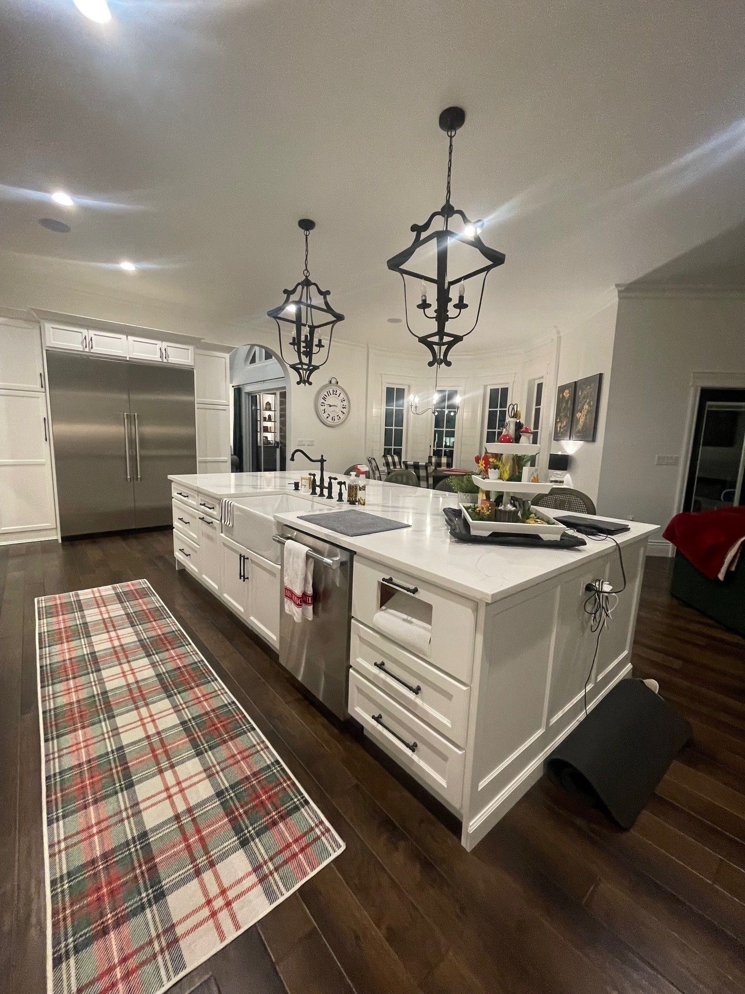 White kitchen island with a cooktop, a plaid rug, and dark wood floors.