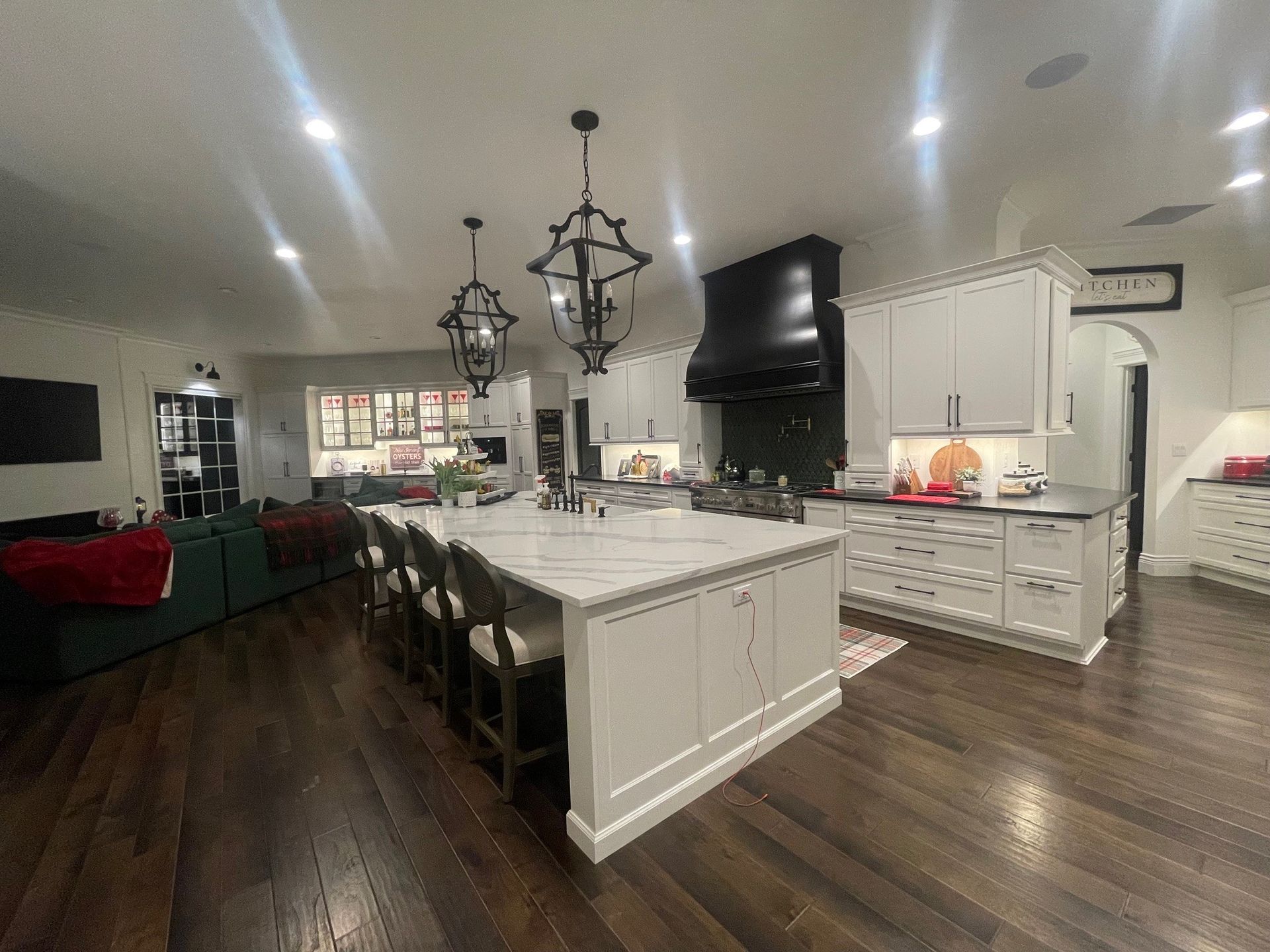 Spacious kitchen with a large island, dark wood floors, white cabinets, and black range hood.