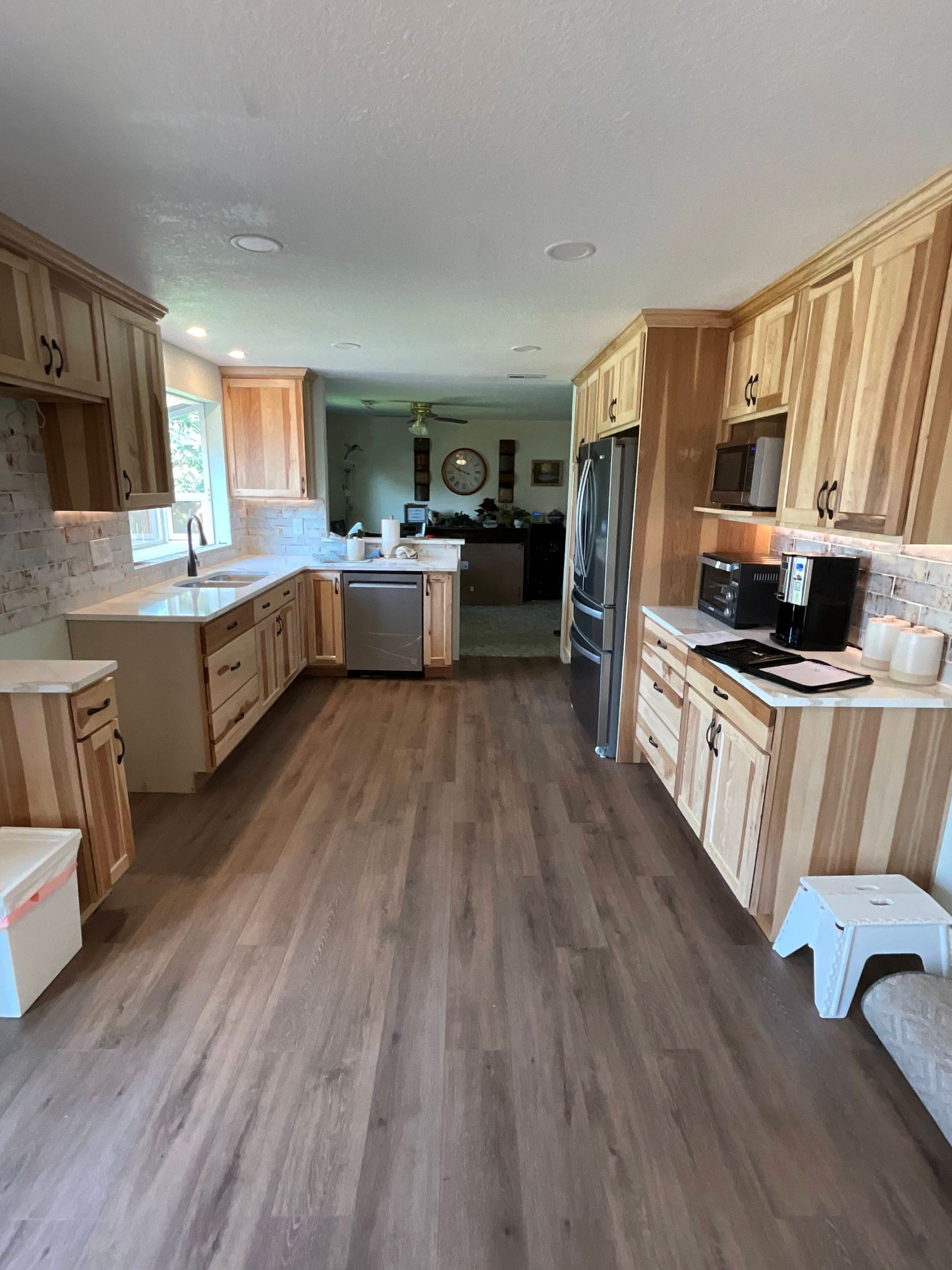 Kitchen with light wood cabinets and flooring, stainless steel appliances, and white countertops.