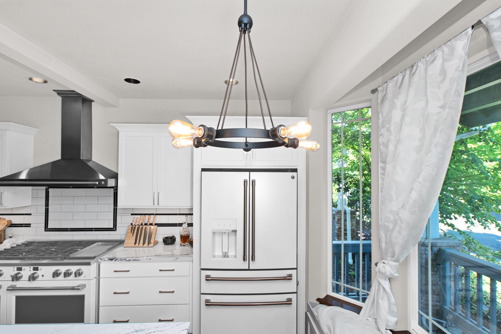A kitchen with white cabinets , a stainless steel refrigerator , a stove , and a chandelier.