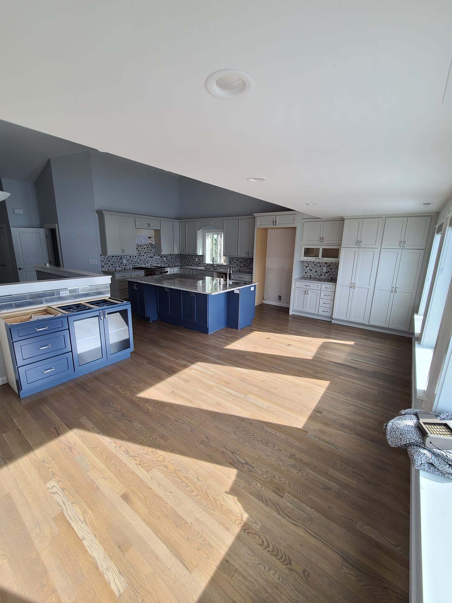 A large room with hardwood floors and a kitchen in the background.