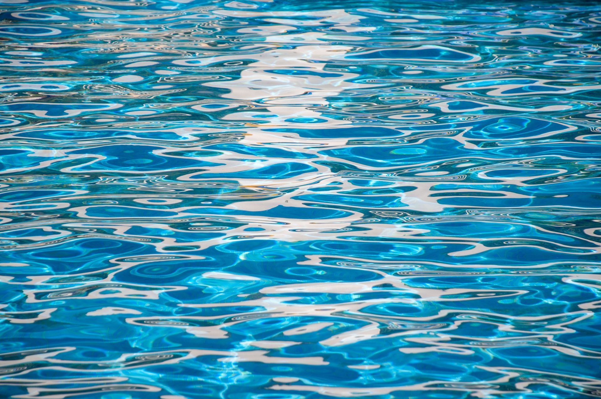 Sunlit rippling blue swimming pool water surface with shimmering reflections on a clear day.