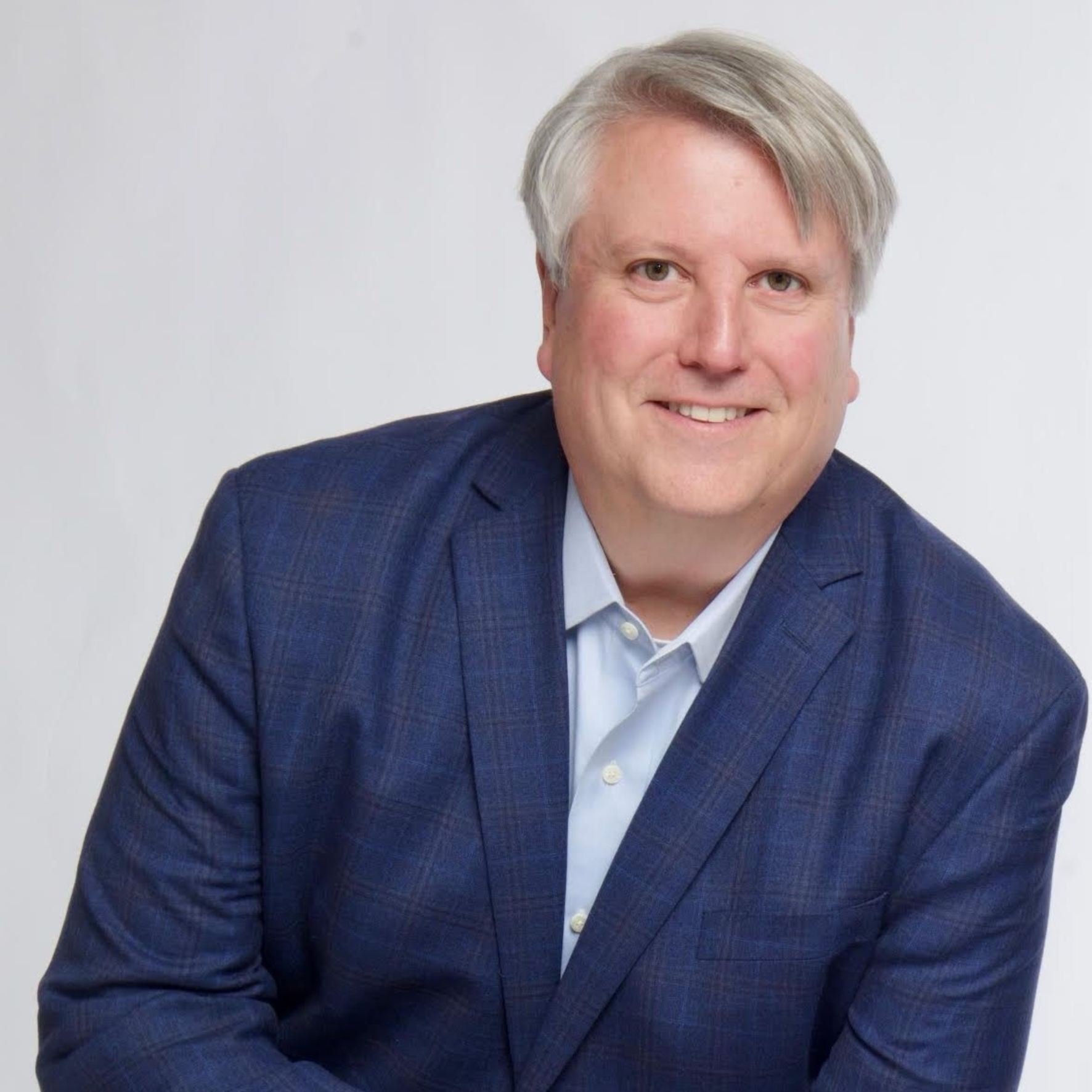 Smiling person in a blue blazer and light shirt against a plain white background