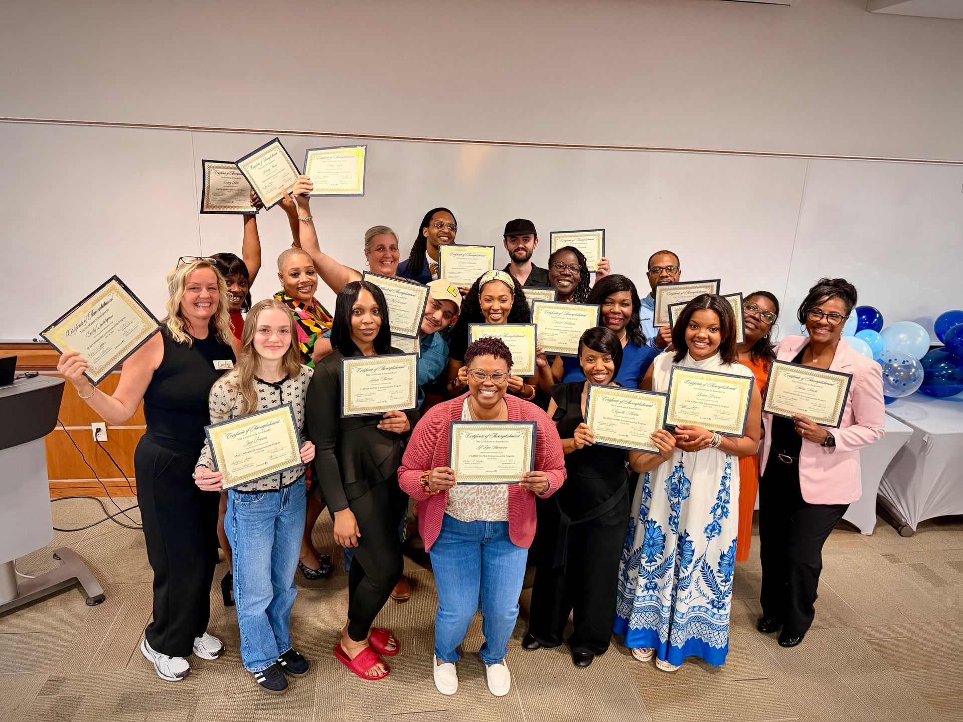 Group holding framed certificates in a room, smiling and posing for a celebration photo.