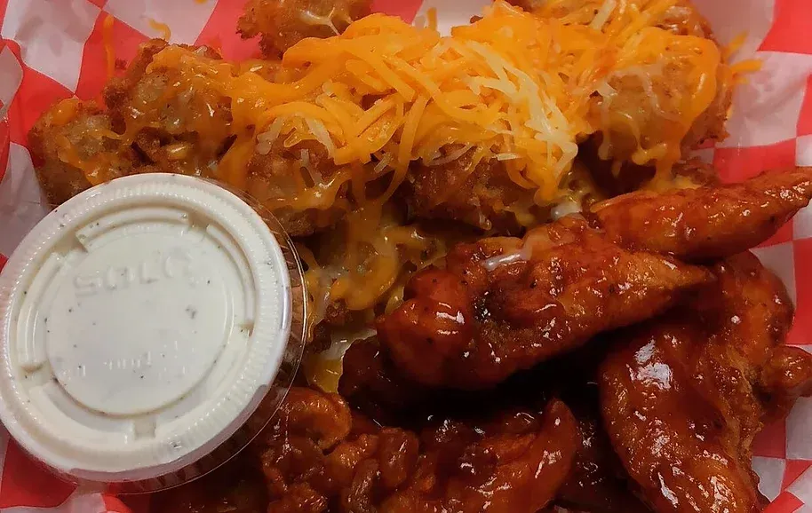 Buffalo wings and fries topped with shredded cheese and served with ranch dressing in a takeout tray