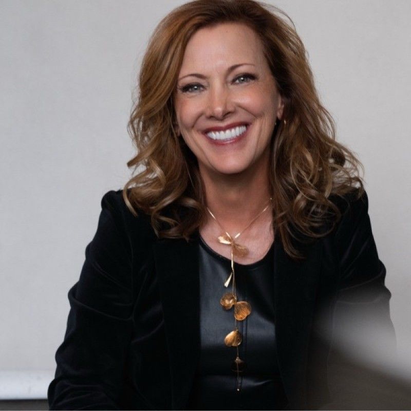 Smiling woman in a black top and blazer against a light gray background