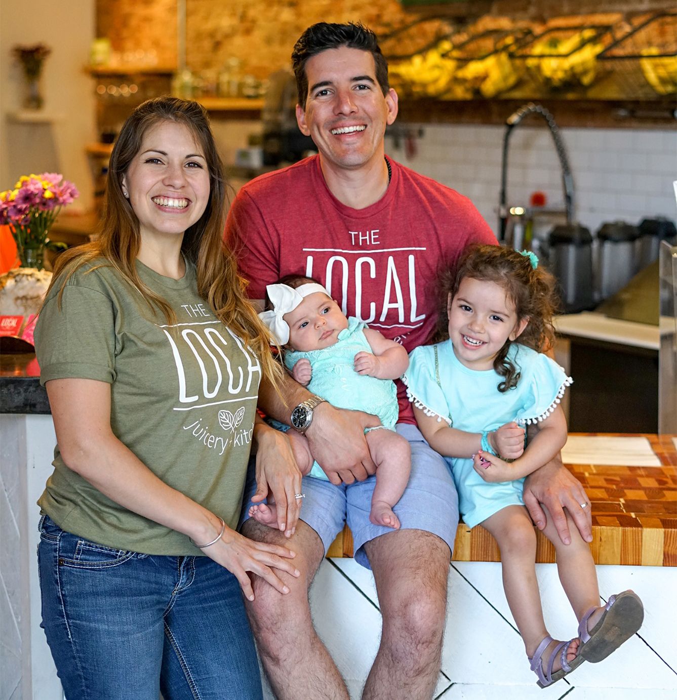 Smiling family of four posing in a kitchen, seated and standing together near the counter