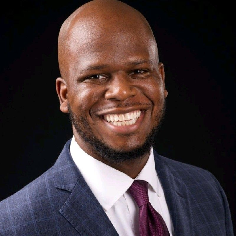 Smiling man in a navy suit and burgundy tie against a dark background