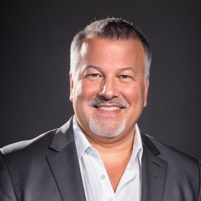 Smiling man in a dark blazer and white shirt against a dark studio background