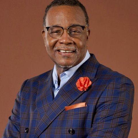 Portrait of a smiling man in glasses wearing a blue plaid suit with an orange lapel flower