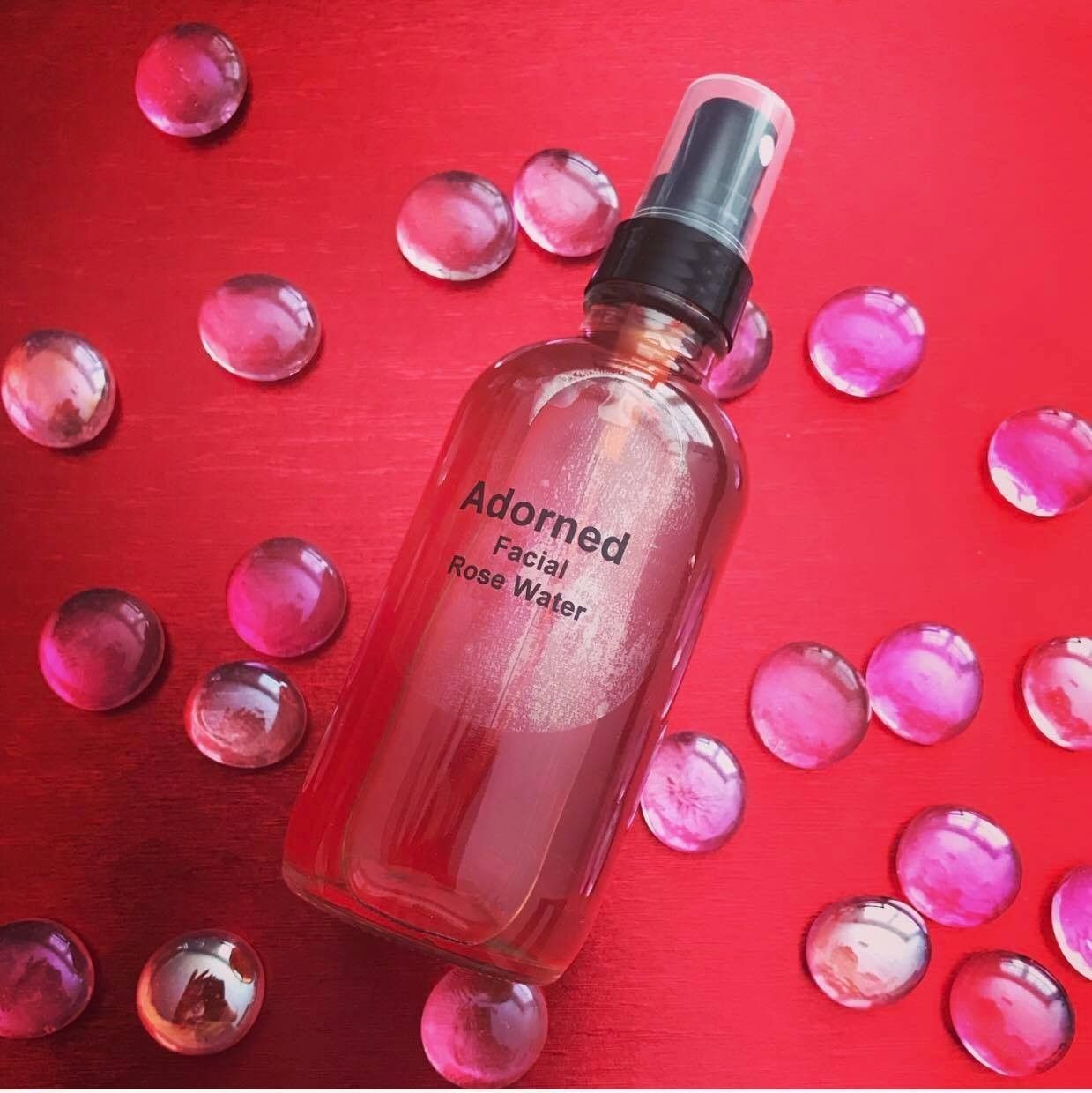 Pink skincare serum bottle on a red background, surrounded by scattered translucent pink beads.
