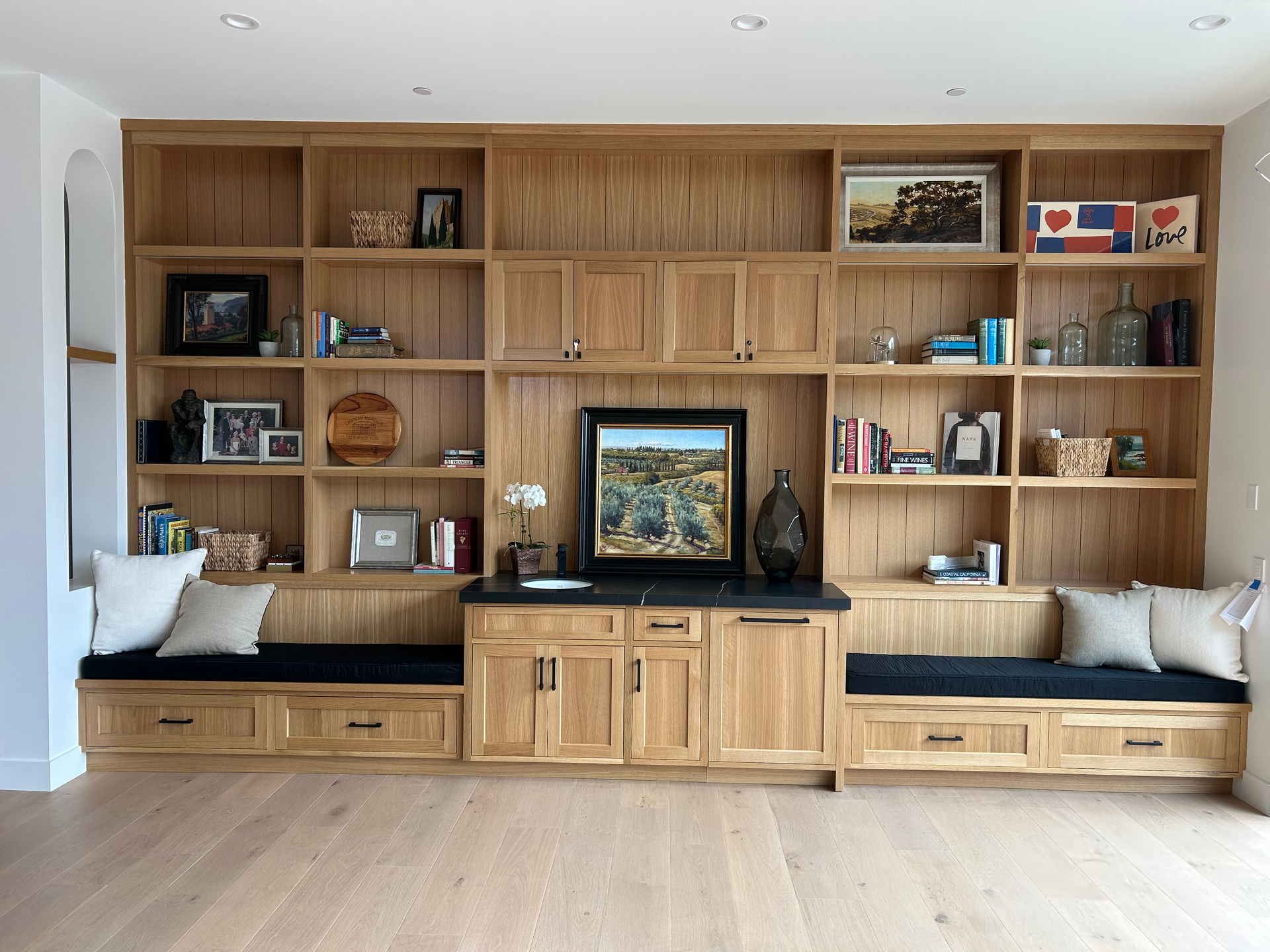 White built-in home office with black countertop, desk area, cabinets, shelves, and a laptop on the left.