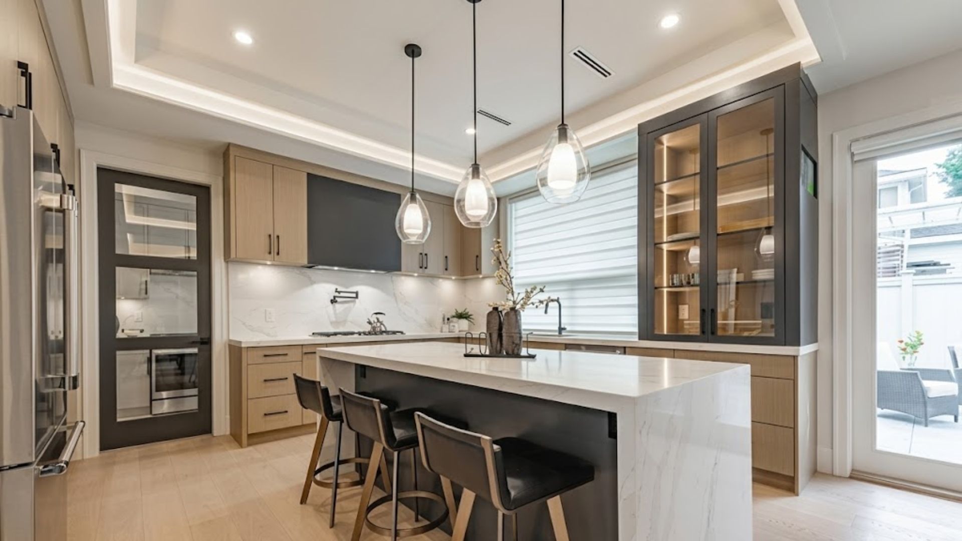 Modern kitchen with island seating, pendant lights, beige cabinetry, and glass-front cabinets