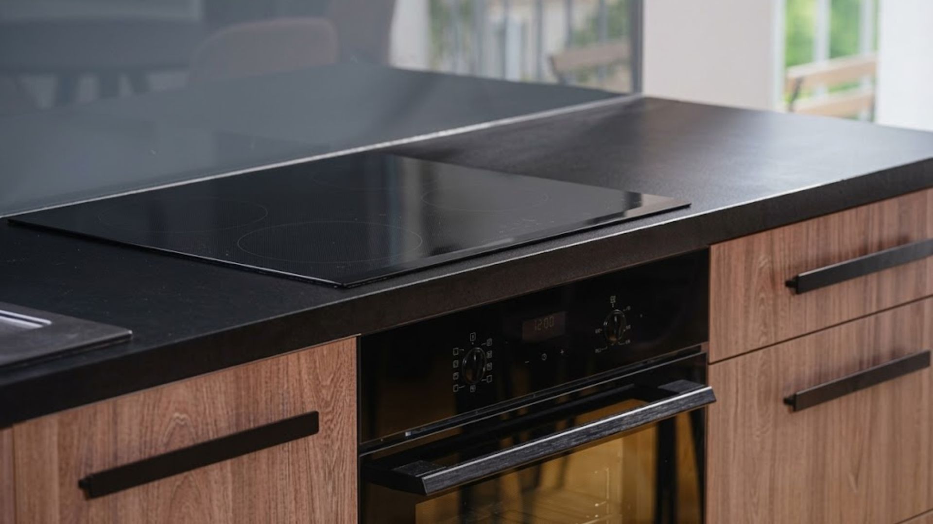 Black induction cooktop with oven in a modern kitchen with wood cabinets and black countertops