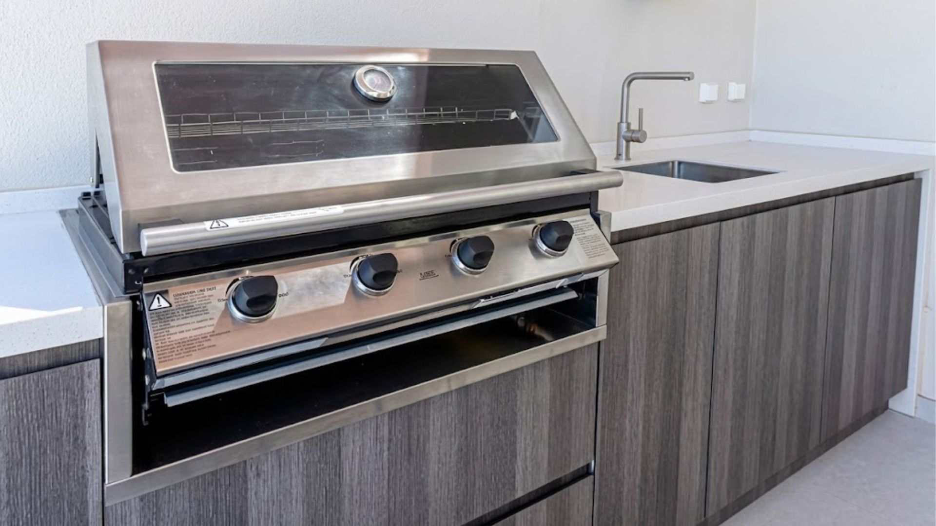 Modern outdoor stainless-steel grill built into a gray wood cabinet on a patio.