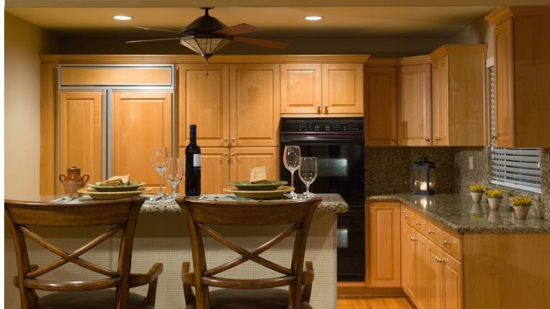 Warm kitchen with wood cabinets, granite island, barstools, and a black oven under pendant lighting