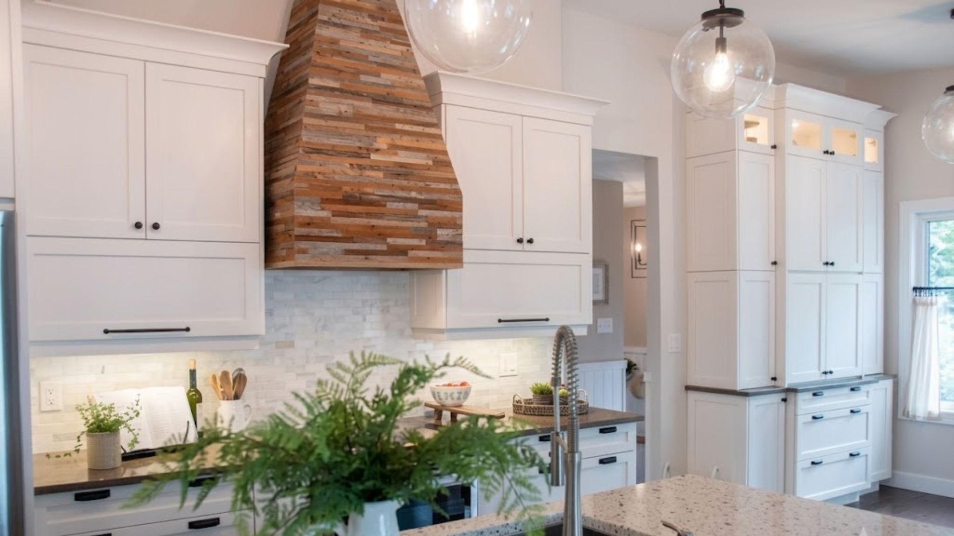 Bright white kitchen with wood range hood, marble island, and pendant lights