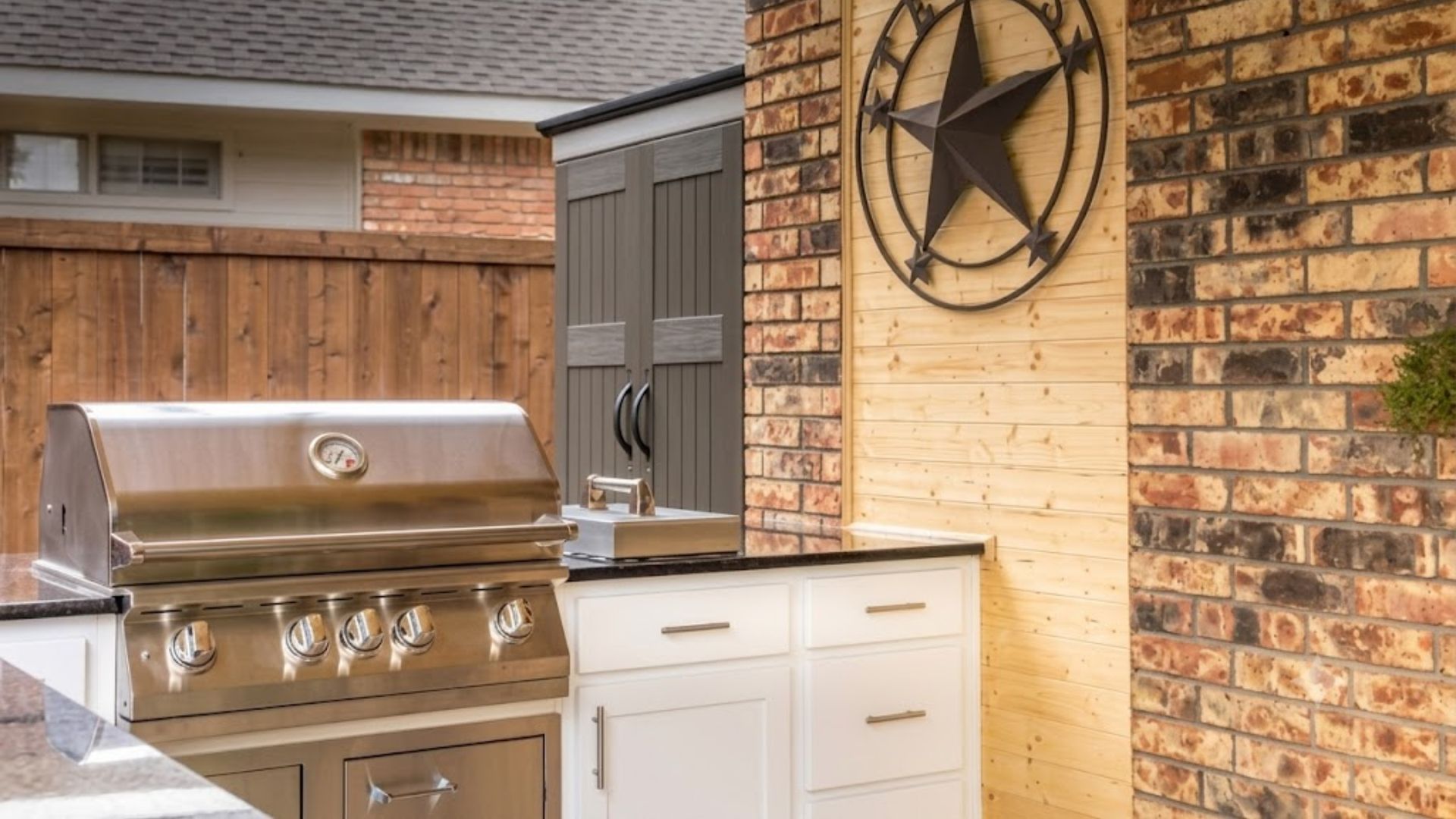 Outdoor brick patio with stainless steel grill, white cabinet, and large metal star wall decor