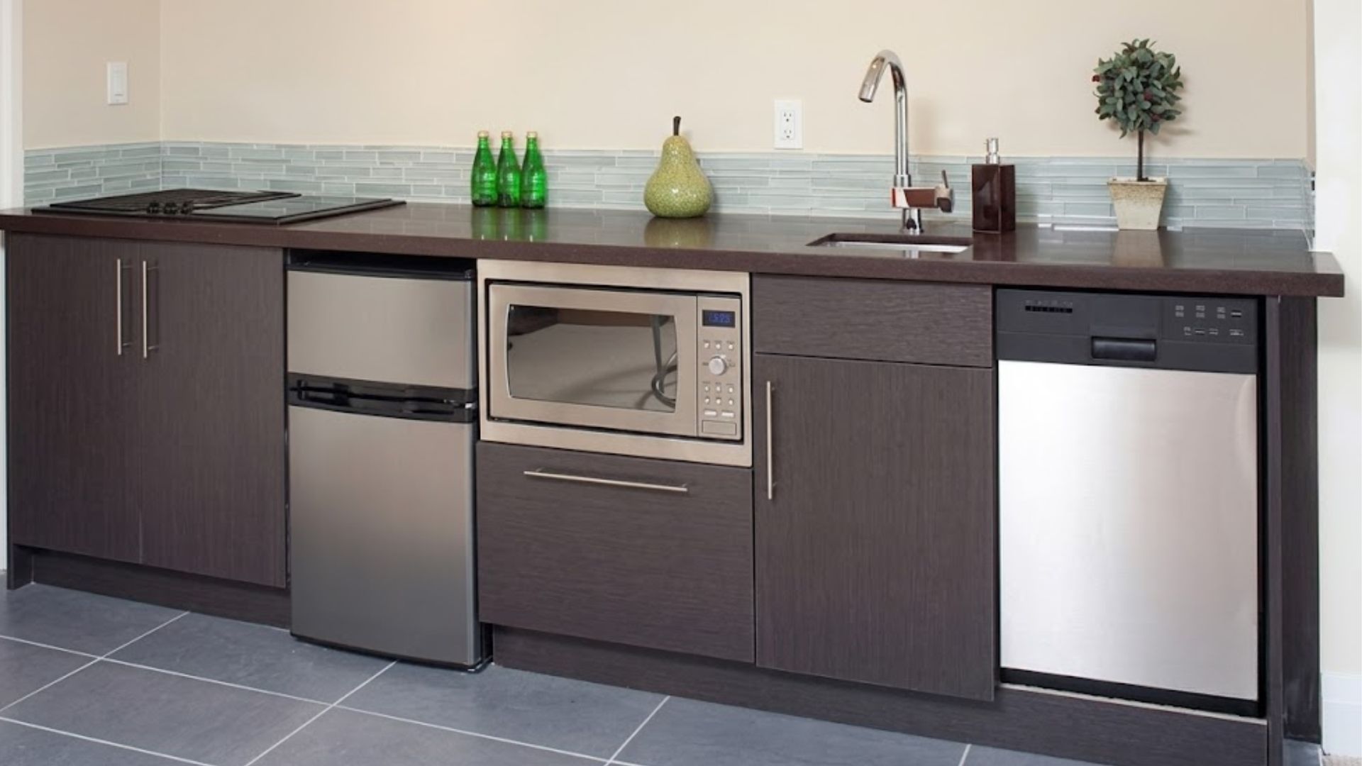 Modern kitchen counter with dark cabinets, sink, microwave, mini fridge, and dishwasher