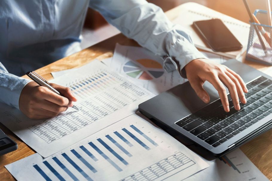 Hands working on financial charts with a pen and laptop on a desk
