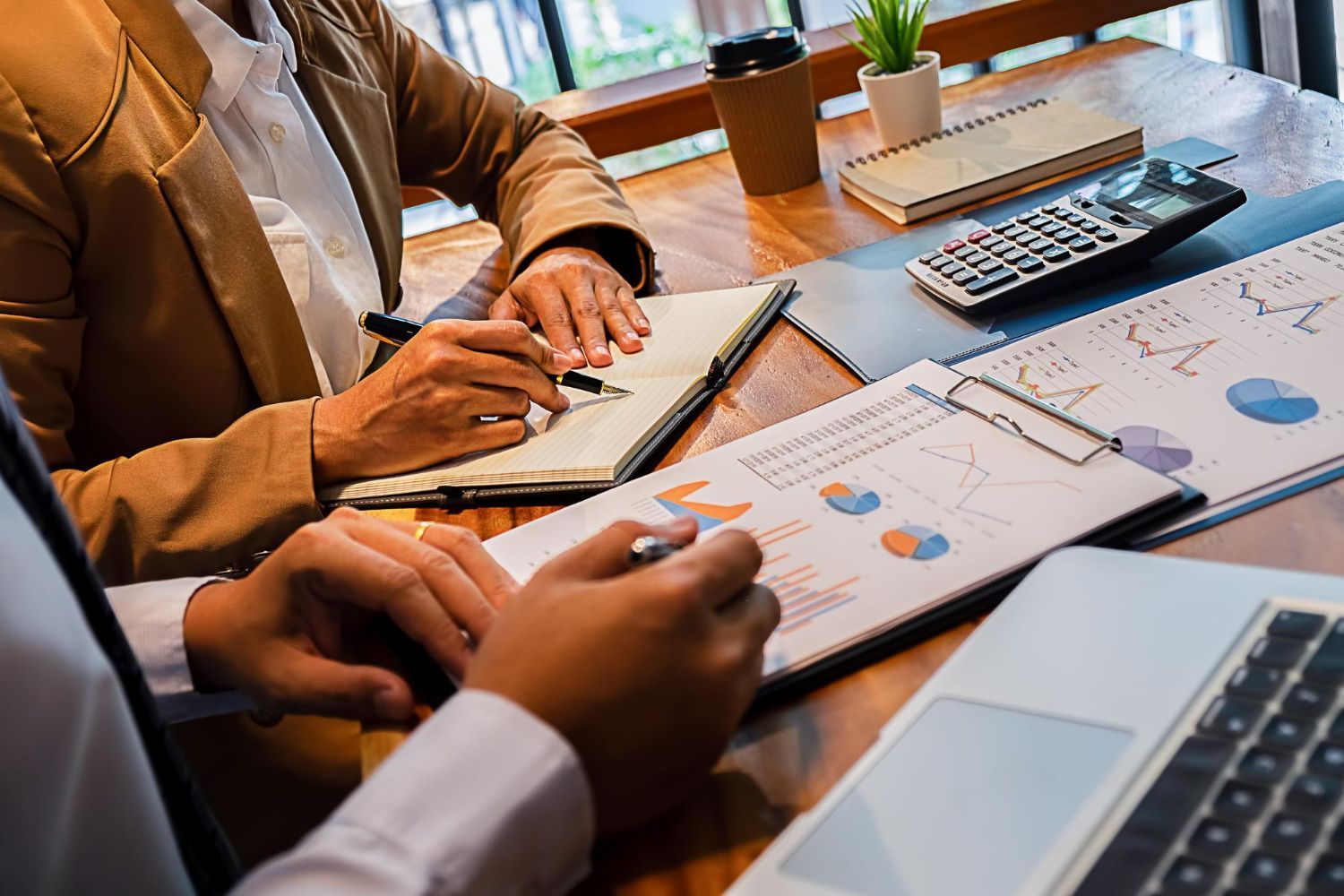 Two people reviewing financial charts at a desk with a laptop, calculator, and paperwork