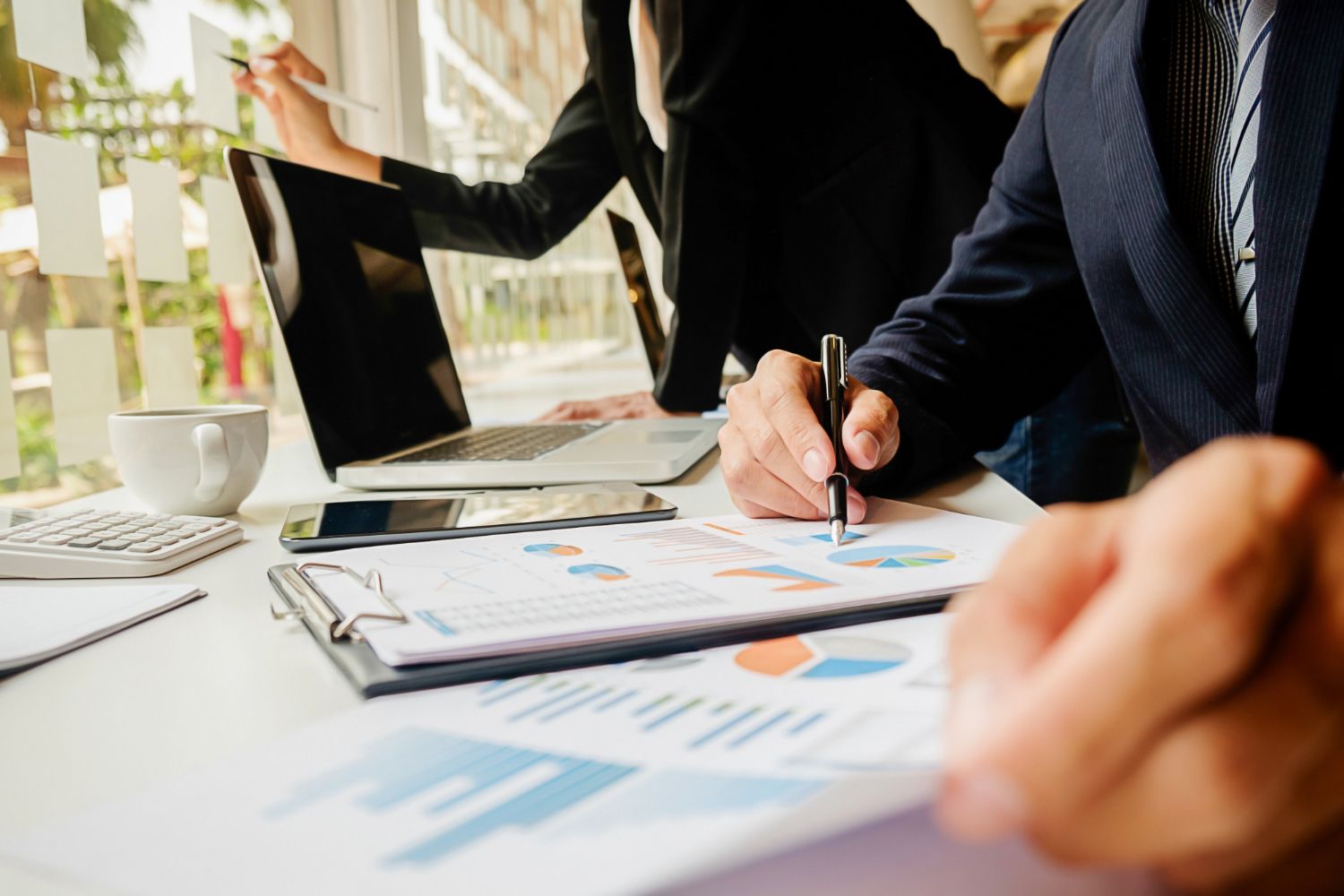Business meeting with hands reviewing charts and documents around a laptop on a conference table
