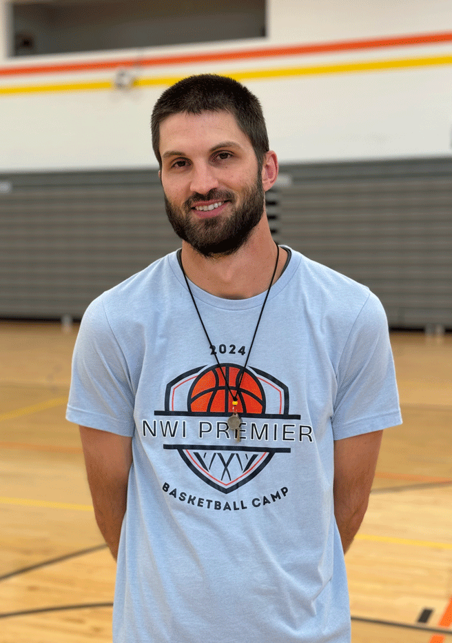 A man wearing a t-shirt with a basketball on it is standing on a basketball court.