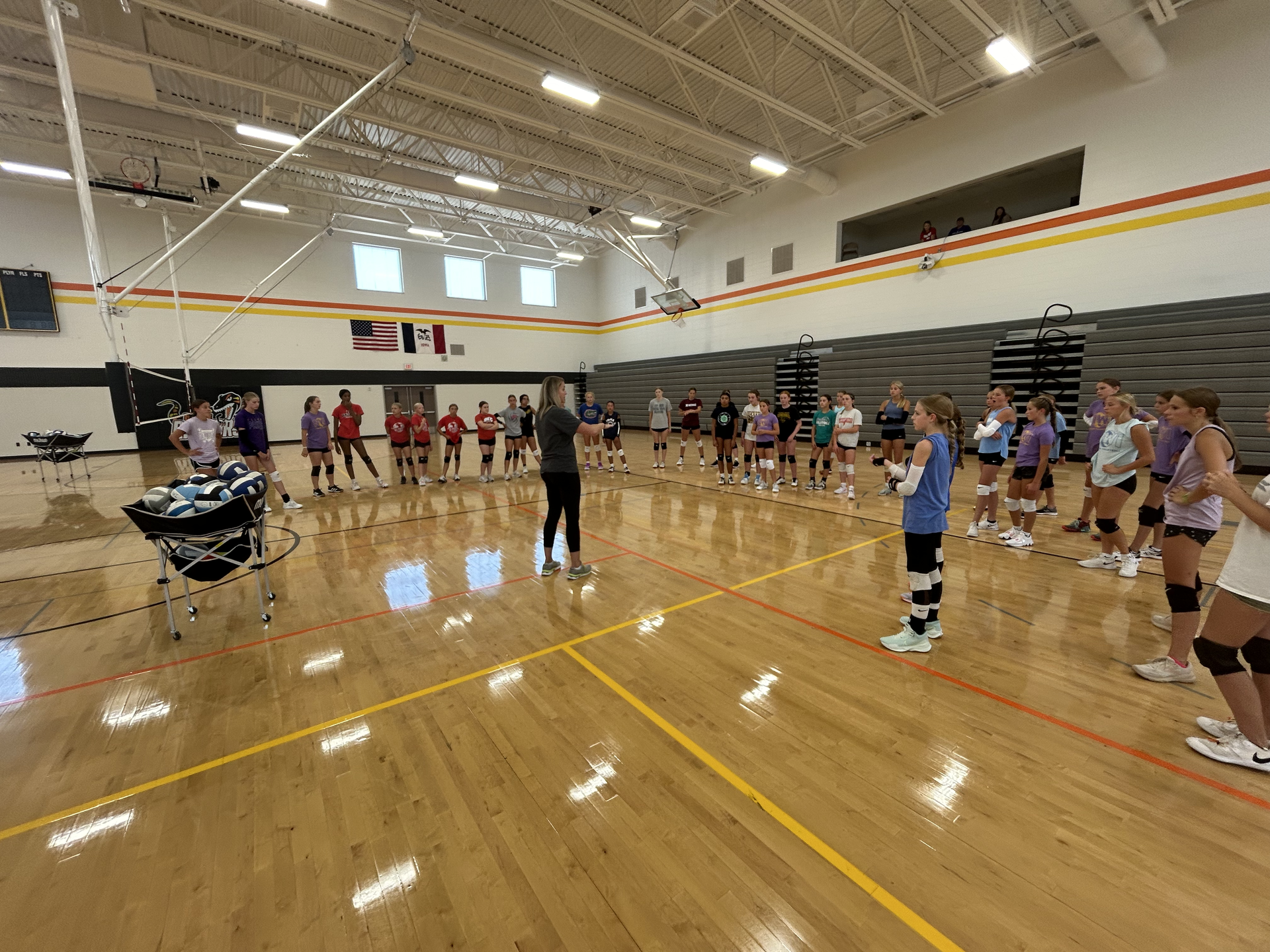 A group of people are standing on a wooden floor in a gym.