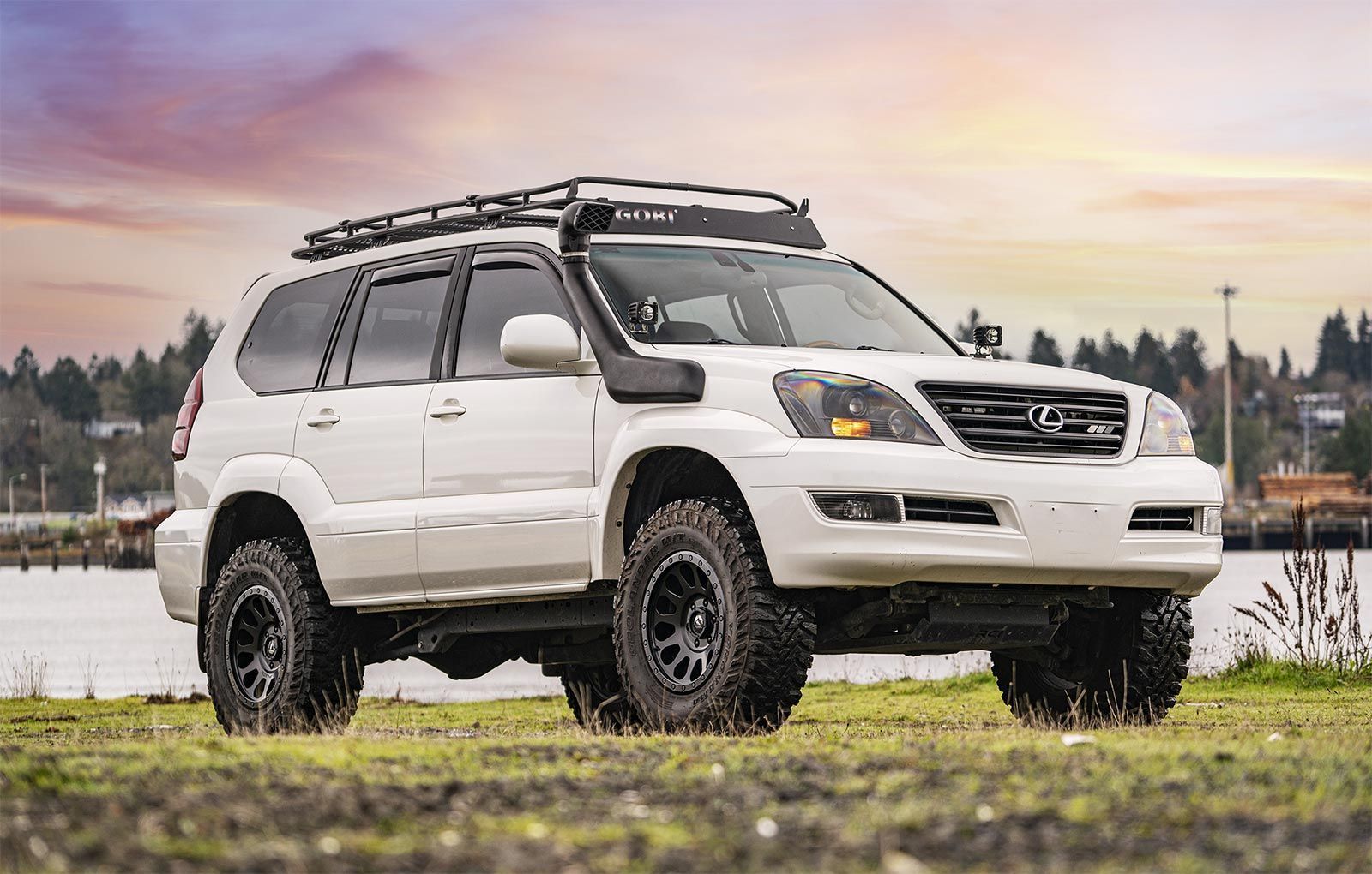 A white suv is parked in a grassy field next to a body of water.