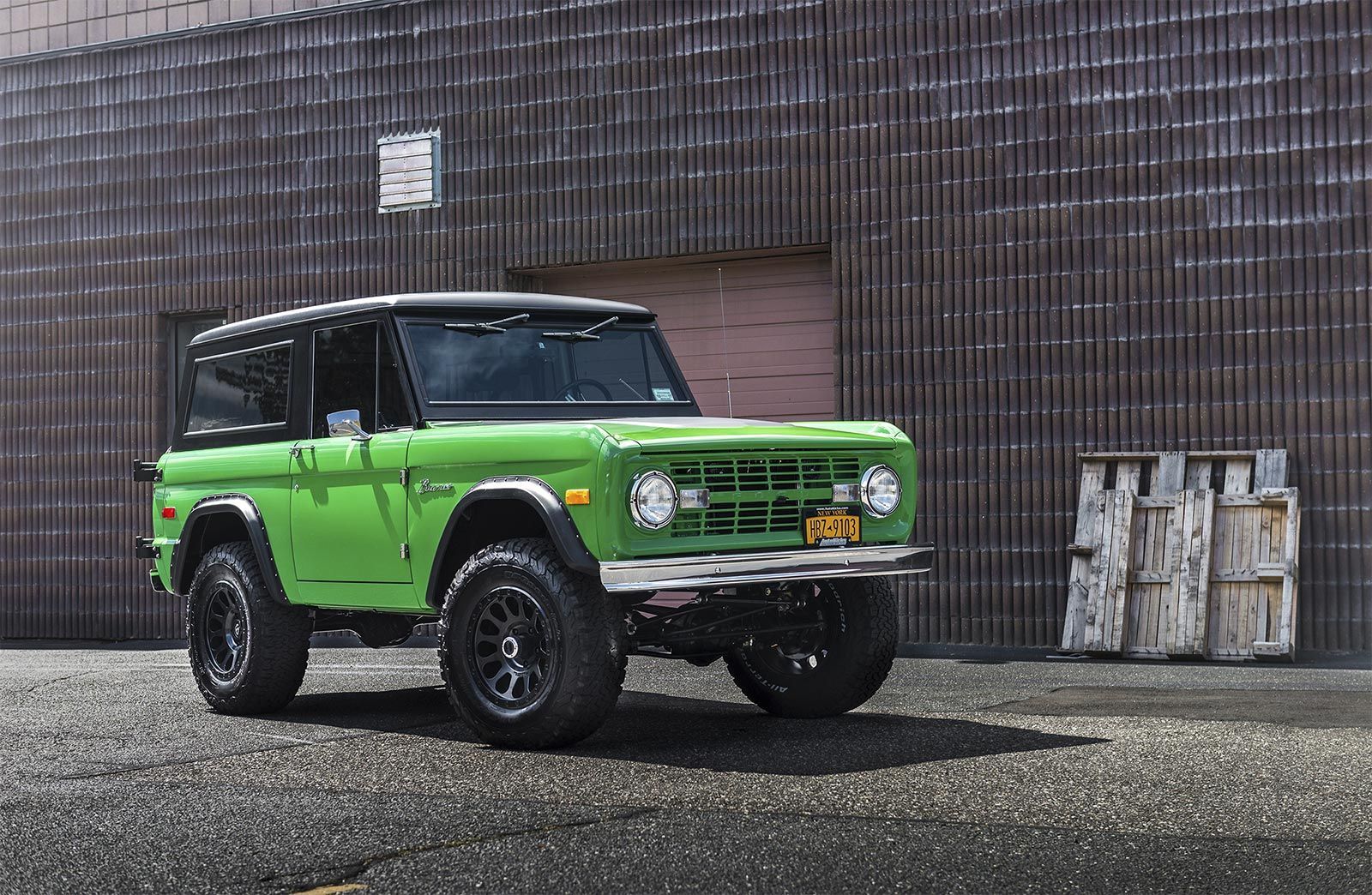 A green ford bronco is parked in front of a brick building