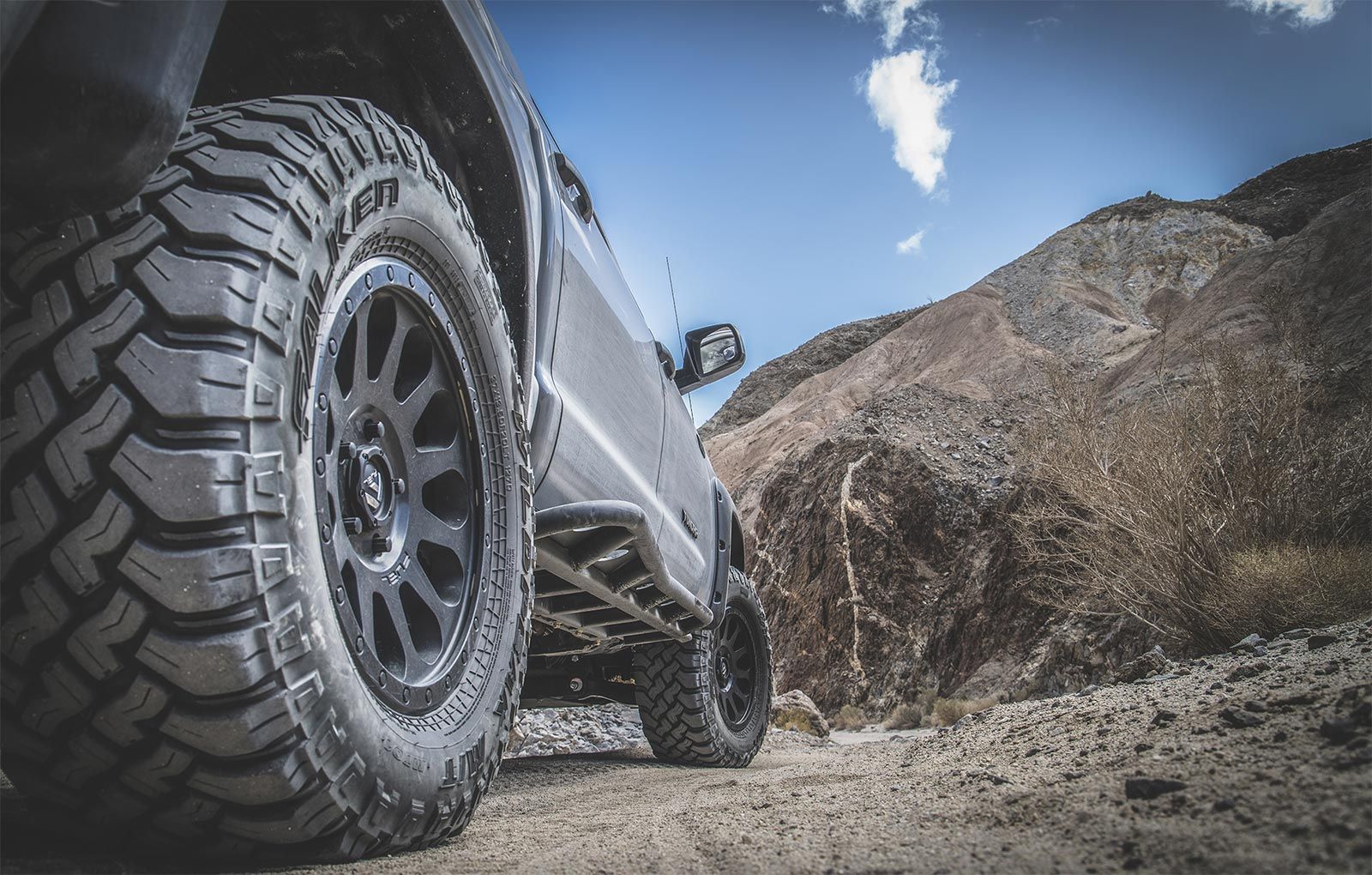 A truck is parked on a dirt road with mountains in the background.