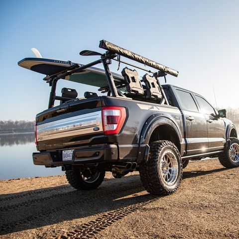 A truck with a surfboard in the back is parked next to a body of water.